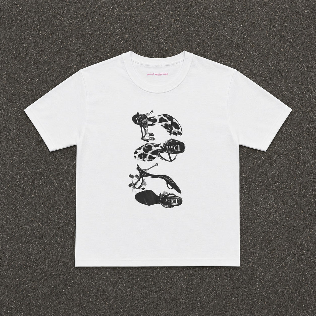 Heels Baby Tee in white, flat lay with a black and white stack of heels print